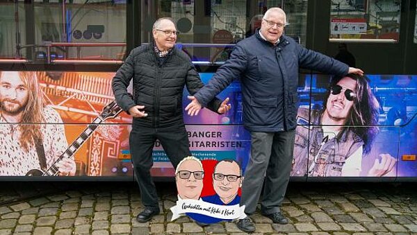 Kurt spielt Luftgitarre und Kübi tanzt vor einem mit Rockern beklebten NightLiner-Bus