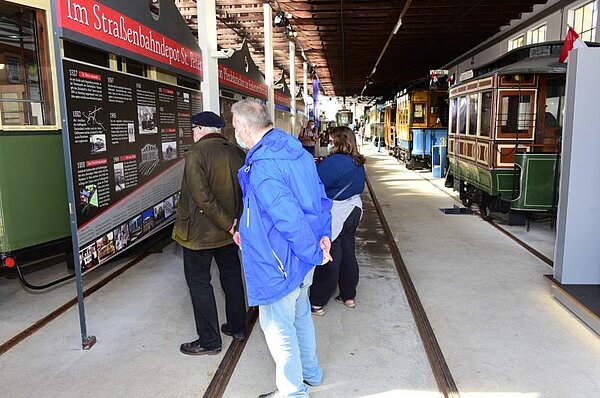 Interessierte Besucher lesen die Infotafel zur Geschichte der Straßenbahn