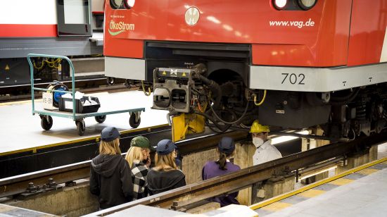 Tobias Schneider führt die Besucherinnen des Girl's Days in der U-Bahn-Werkstatt in eine Grube unter einem Zug