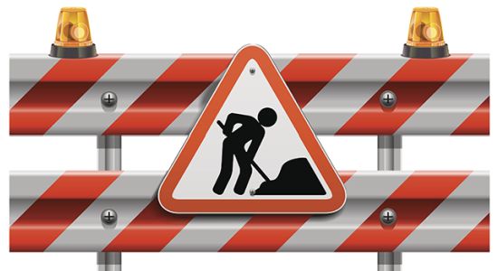 Rot-weiß gestreifter Bauzaun mit dem Verkehrsschild "Achtung Baustelle" im Vordergrund